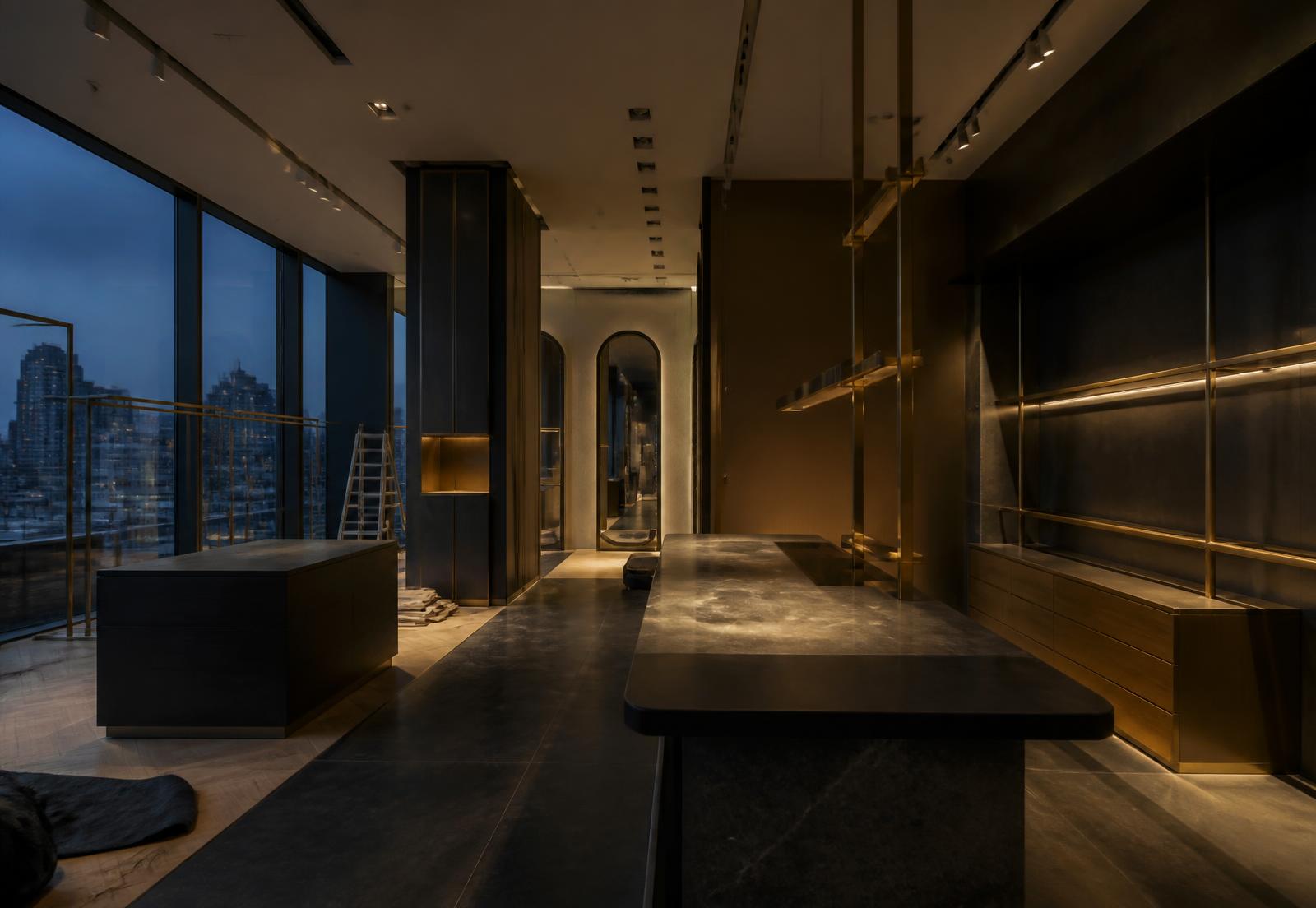 Retail interior mid-fit-out at dusk, lit in warm brass tones